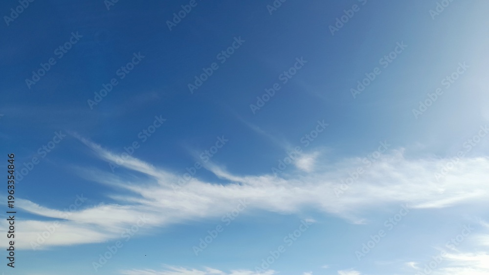 Obraz premium Wispy white cirrus clouds on a clear bright blue sky background on a sunny day.