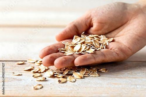 Hand holding a handful of organic oat flakes over a wooden table, healthy breakfast concept.