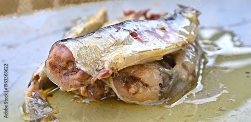 Top view of sardines in yellow oil spilled on grey metal surface.