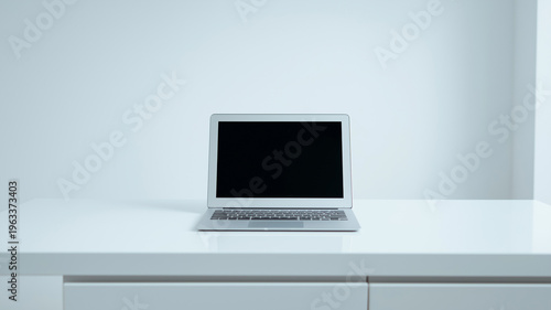 シンプルな白いデスクに置かれたノートパソコンのミニマルなワークスペース背景