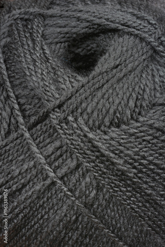 A close up view shows the soft texture of a ball of black knitting yarn with interwoven fibers