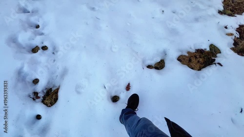 First-person perspective of a person walking across patches of snow and dry grass.