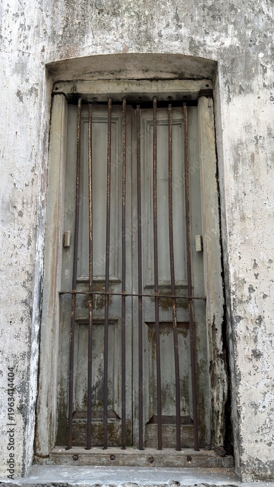 Obraz premium This image features an old wooden window secured with rusted metal bars in a distressed wall