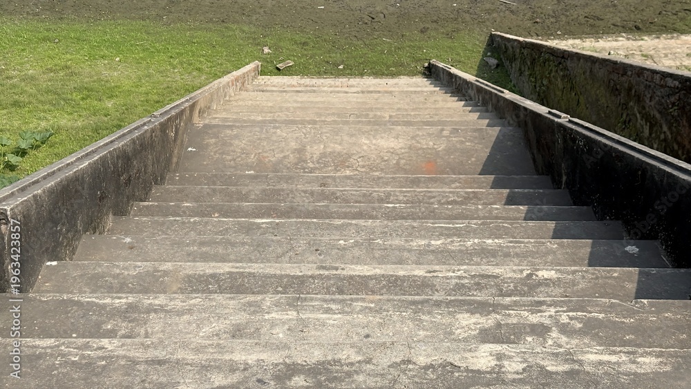 Obraz premium Weathered Concrete Steps Descending Towards a Grassy Embankment and Muddy Shore