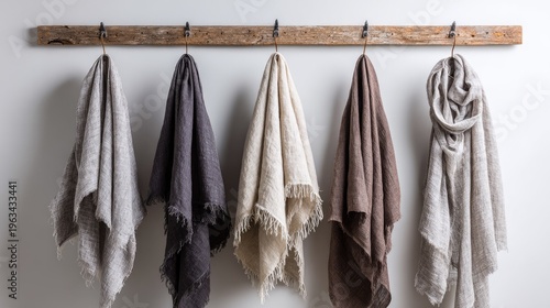 Assortment of five draped linen textiles displaying neutral color variations hangs from rustic wooden hardware against a light wall.