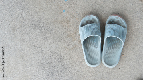 Top view of a pair of used light blue rubber slides or slippers placed on a textured grey concrete floor with copy space.