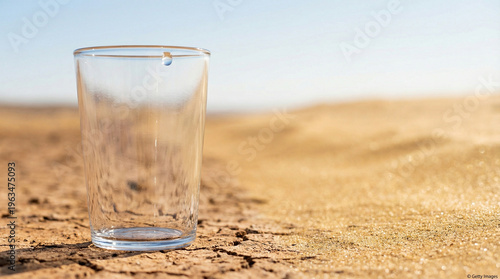 Empty glass standing on dry cracked earth in a desert. Concept of water scarcity, global warming, drought, and environmental crisis. Visual metaphor for thirst and lack of vital resources.
