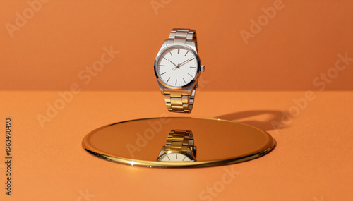 Silver-toned wristwatch hovers above oval mirror on monochromatic tangerine background with warm sidelight creating distinct shadow.
