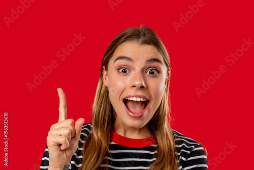 Happy woman having idea eureka moment, pointing finger up on red background. Clever lady showing answer gesture or remembered what she forgot, memory concept.