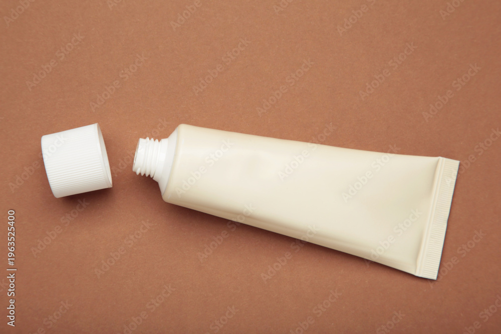 Fototapeta premium Beige tube of cream on brown background. Mockup plastic tube for cosmetics