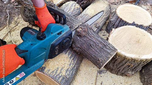 Hand holds chain saw with battery to trim broken branch of an tree. Modern work with electric portable brushless cordless chain saw.