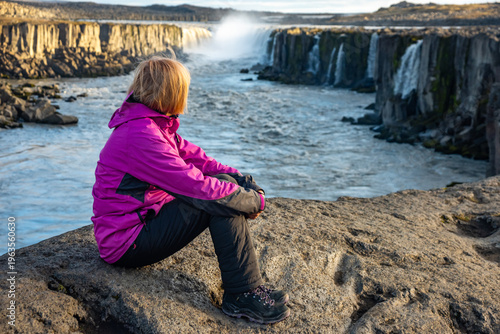 Witness the majesty of Selfoss waterfall in Iceland, as a visitor enjoys the scenic views along the riverbank surrounded by nature