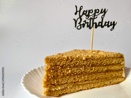 a piece of delicious cake on a white plate on a white background, happy birthday greetings