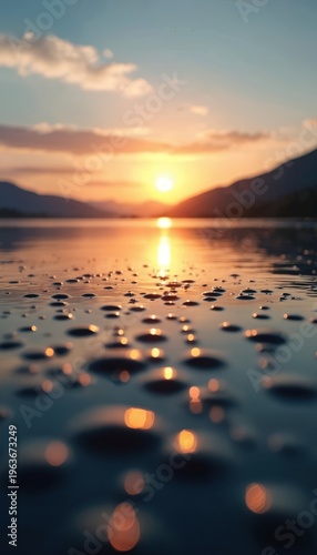 Low angle sunrise over calm water surface with ripples and sun reflection. Mountains outline distant horizon at dawn. Peaceful nature scene.