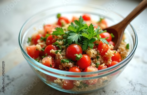 Close-up glass bowl with tabbouleh salad. Cherry tomatoes, bulgur, parsley mix in healthy vegetarian dish. Wooden spoon stirs fresh ingredients for lunch or dinner.