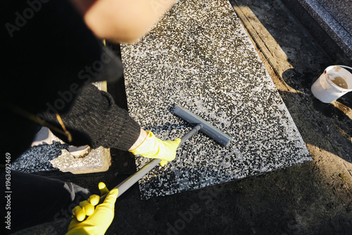 Tableau sur toile Person cleaning gravestone with tool and gloves