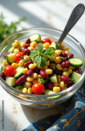 Fresh bean salad with corn, tomato, and cucumber served in glass bowl. Healthy mixed vegetable and legume dish with parsley garnish. Ready to eat meal in studio light.