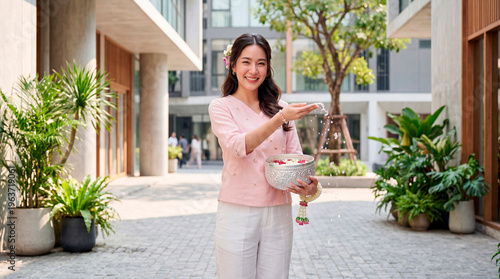 A woman with a basket of plants in her hands at the Songkran festival amidst urban greenery and sunlight