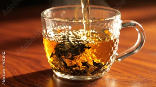 Hot water pouring into clear glass mug with tea leaves