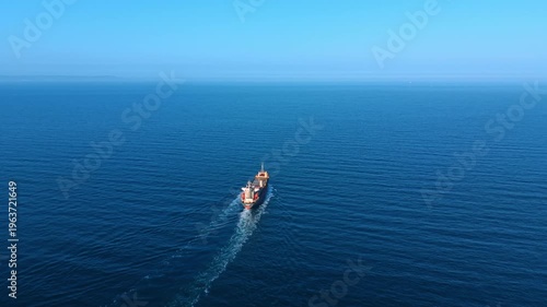Top down aerial shot of ship in ocean. Perspective of a cargo vessel sailing in deep blue sea.