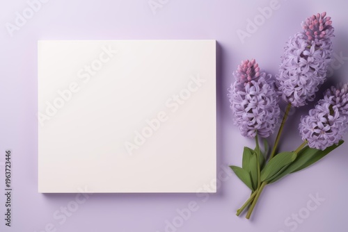 Blank note with purple hyacinth flowers creating a flat lay on a lilac background
