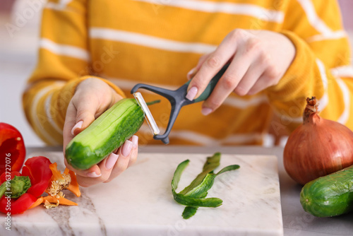 Tableau sur toile Woman peeling fresh cucumber at grey table with vegetables indoors, closeup