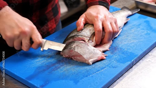 Person filleting fresh fish with a knife on blue cutting board