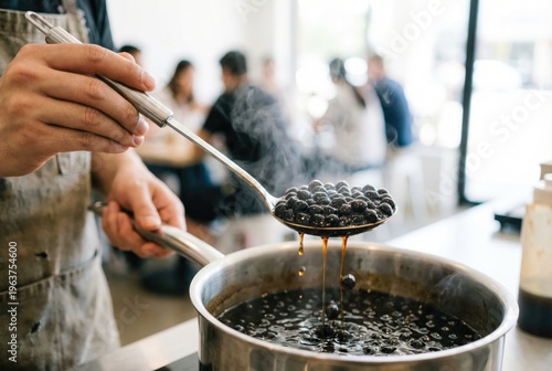 Barista using a strainer spoon to scoop hot black tapioca pearls out of a boiling pot of sweet syrup