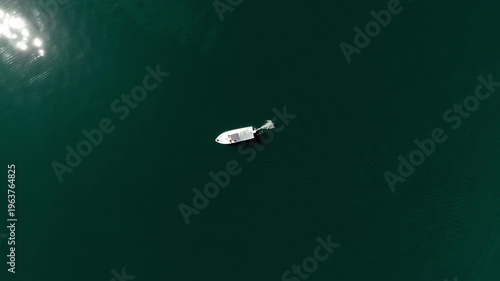 Small tourist boat adrift in vast azure ocean, captured in a minimalist composition with endless water surrounding it, sunlight shimmering across the surface and creating soft reflections and tranquil