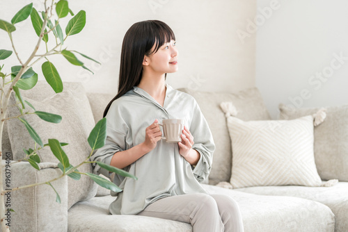 Bild auf Leinwand An Asian woman relaxes at home in the morning, drinking tea or hot water from a mug (a way to promote warmth)