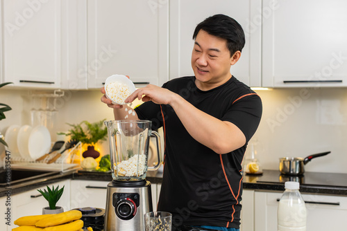 Asian man pours cottage cheese into blender with banana preparing smoothie or protein shake for breakfast. Powerful protein drink supports clean diet weight control fitness energy and daily wellness.