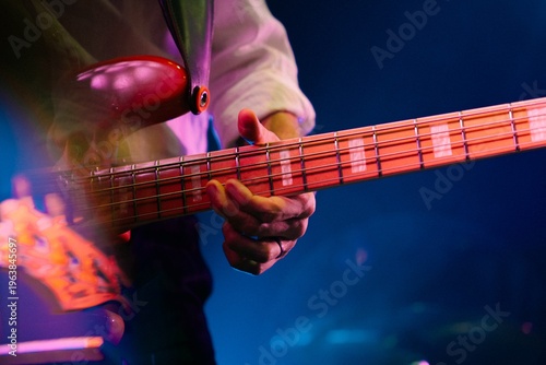 Close-up of hand playing red electric bass guitar under stage lights