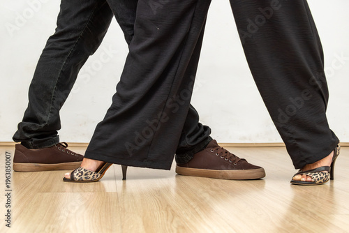 Detalhe de passos de dança entre duas pessoas com salto alto e tênis em piso de madeira