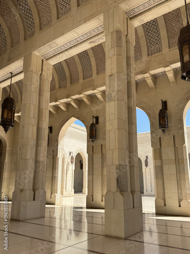 Marble arcade of grand mosque with columns and lanterns in sunlight, Oman