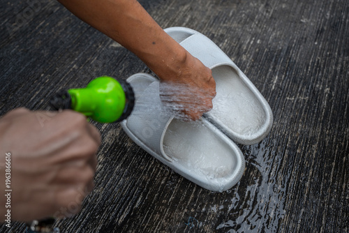 people washing rubber slippers with water hose and plastic brush, cleaning on house yard, natural background