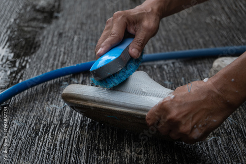 people washing rubber slippers with water hose and plastic brush, cleaning on house yard, natural background