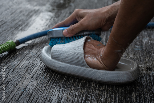 people washing rubber slippers with water hose and plastic brush, cleaning on house yard, natural background