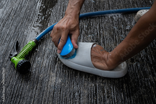 people washing rubber slippers with water hose and plastic brush, cleaning on house yard, natural background
