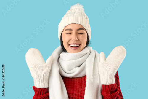 Happy young woman in winter clothes on blue background