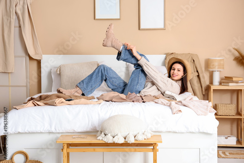 Young woman with scattered clothes lying on bed in room