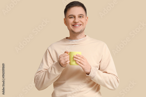 Handsome young man with mug of tea on beige background