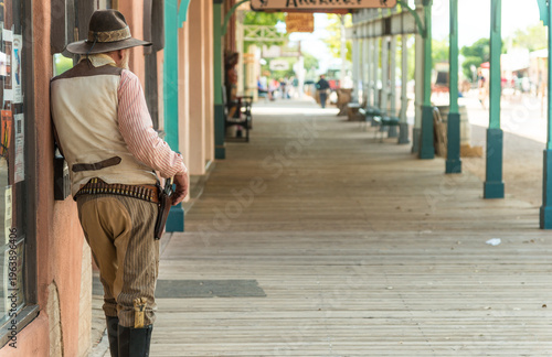 USA, Arizona, Tombstone.  Gunslinger slouching against building on covered boardwalk.