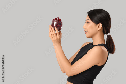 Beautiful Asian woman with sweet cherries on grey background