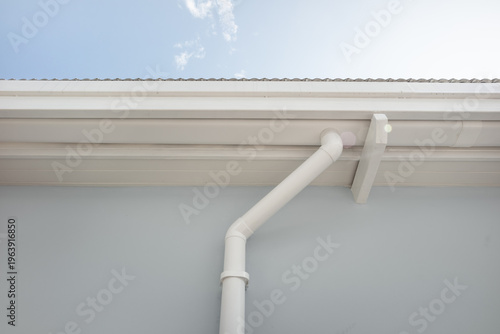 Perspective of white rain gutter system attached to building exterior. Ideal as background for technical content, product promotion and educational materials, modern rainwater drainage solution.