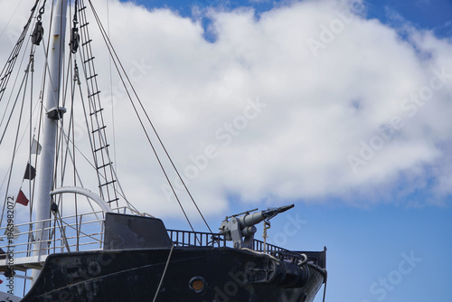Foto Historic black ship bow with prominent mast, rigging and a deck gun against a bl
