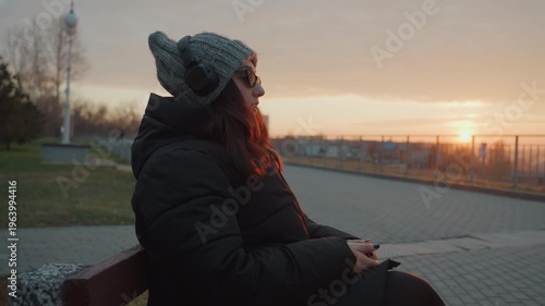 Woman enjoys music during peaceful evening dance. Quiet woman dances gracefully amid sunset in city park. Tranquil female figure sways to melodic tunes against urban sunset scenery at dusk