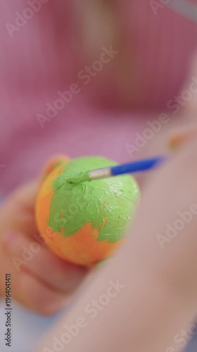 Child's small hands paint a globe with green paint. They brush carefully, covering the sphere's surface. Joyful, focused activity in a creative arts setting. Ideal for education, crafts