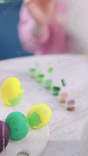 Soft focus shows hands painting eggs. Colorful eggs sit beside paint pots. Childly joy emerges from playful creativity. Perfect for Easter or craft projects