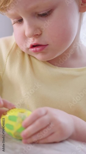 Young child holds colorful egg with curiosity. Eyes widen slightly, showing quiet wonder. Soft light highlights gentle expression. Perfect for family, parenting, or childhood themes