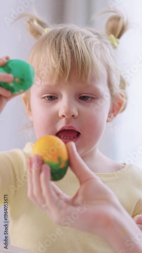 Cute child holds colorful painted eggs. Child smiles while playing with festive Easter eggs. Soft sunlight highlights joyful, curious expression. Perfect for holiday, parenting, or family themes